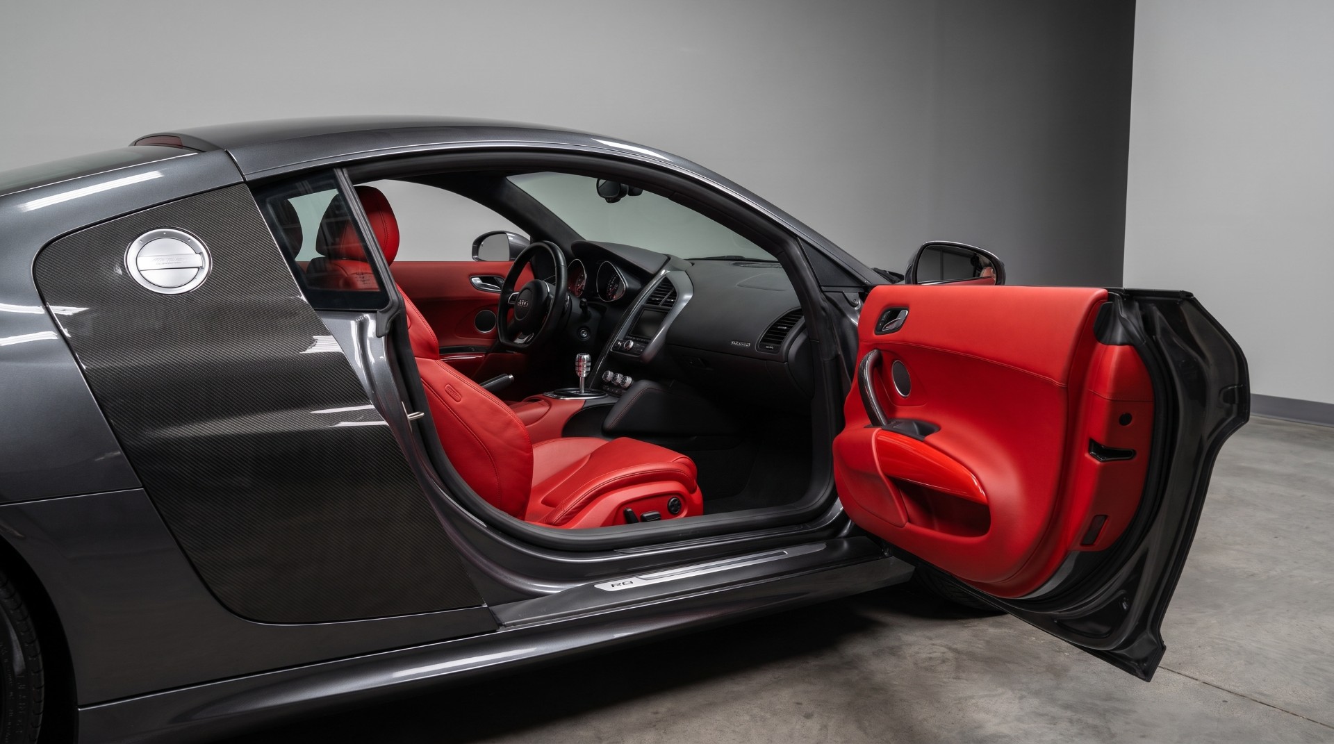 Audi R8 grise à lame carbone, portière ouverte révélant l'intérieur en cuir rouge